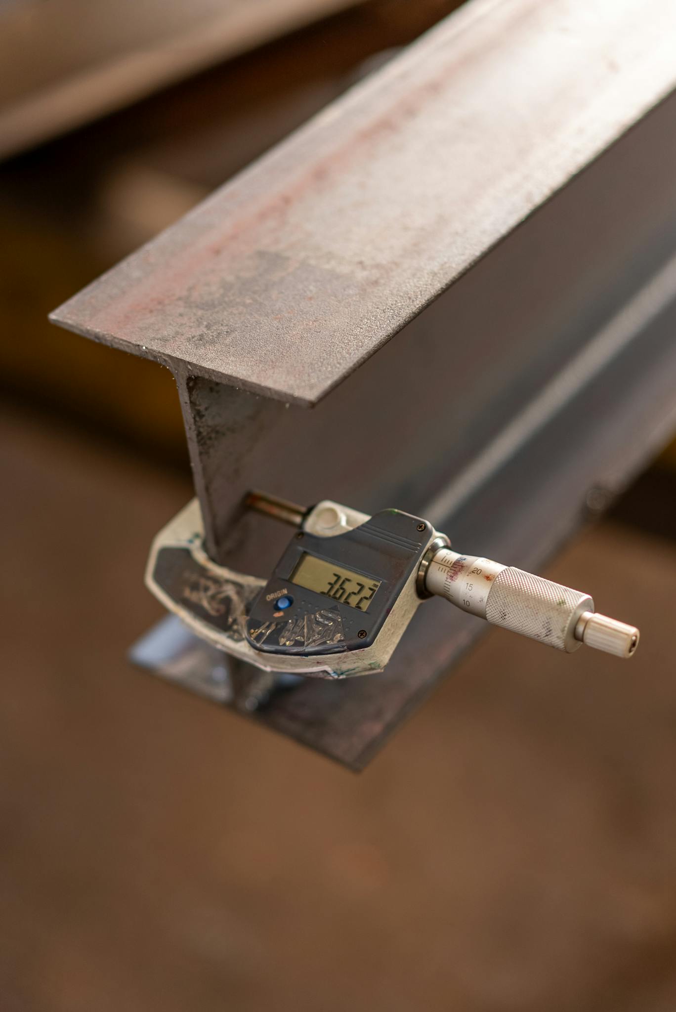 Close-up of an industrial caliper measuring the thickness of a steel beam in a workshop.